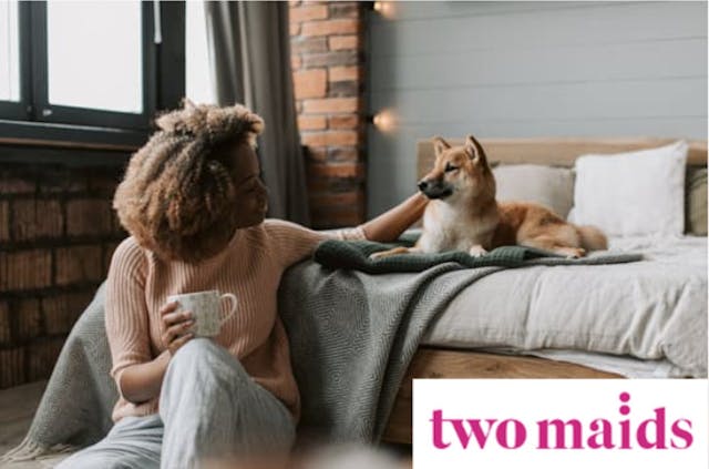 woman holding coffee mug and petting a dog that is laying on bed 